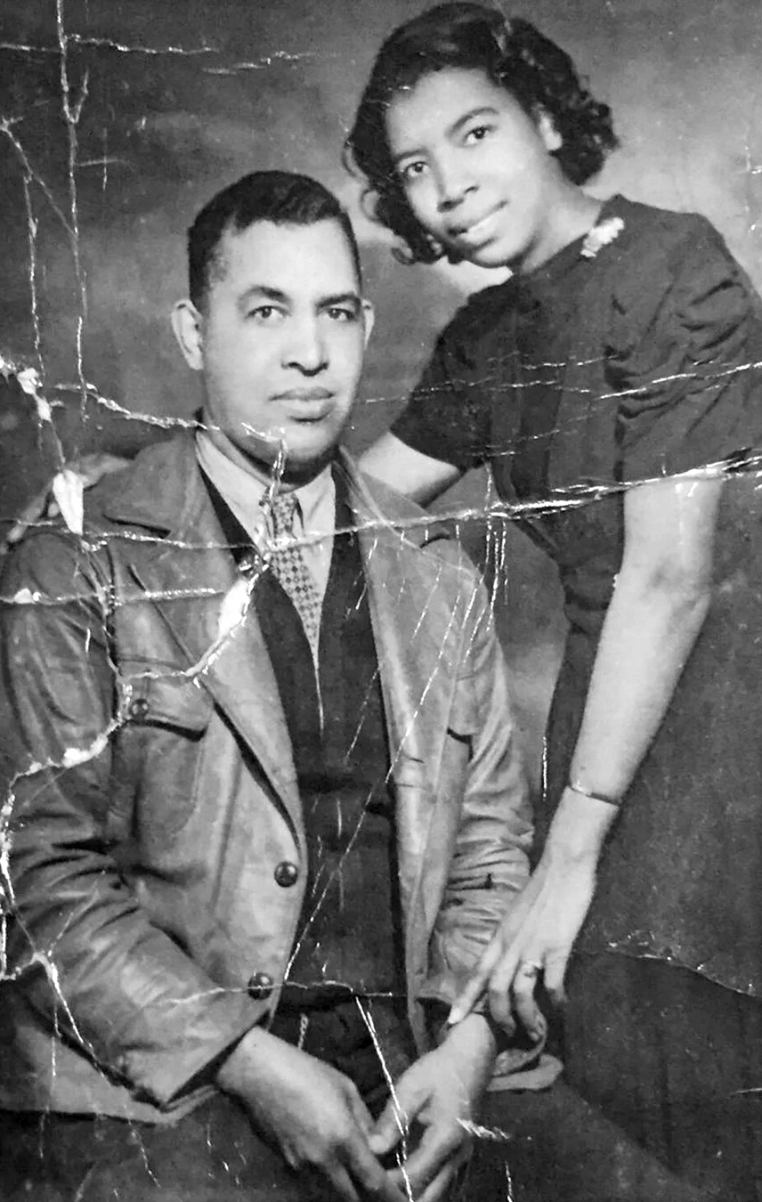 Isadore Banks seated in leather coat and Muriel Banks standing with arm around his shoulder