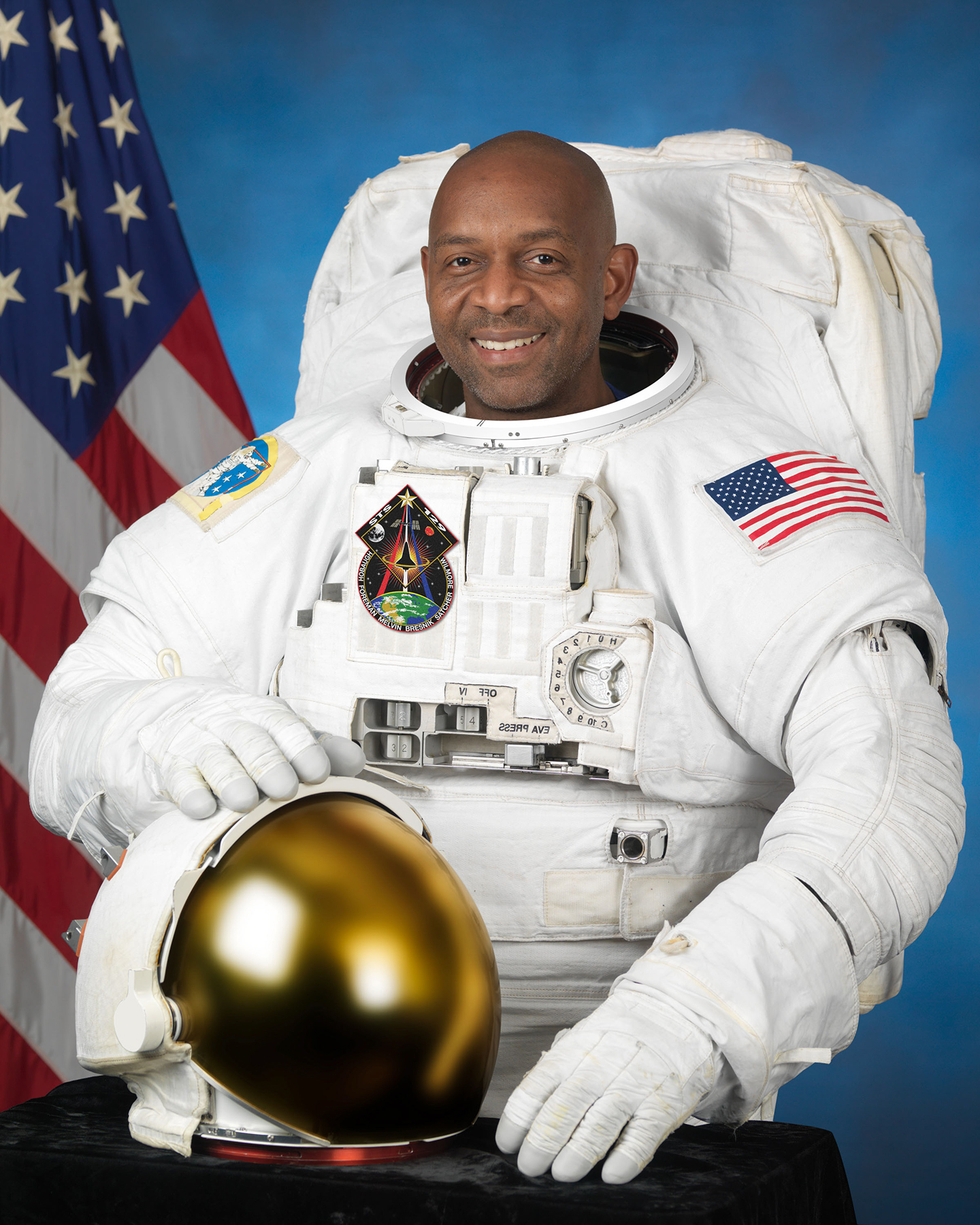 Satcher posing in space suit in front of American flag