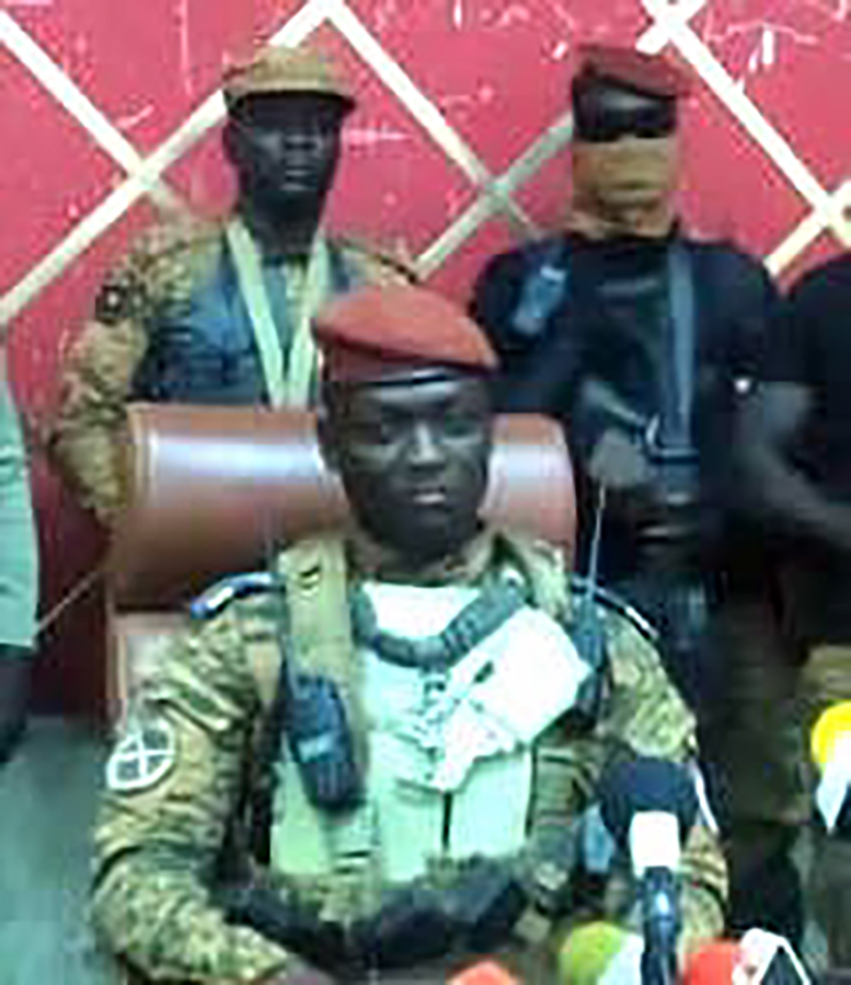 Captain Ibrahim Traoré sitting in a brown leather chair with two armed guards in the background