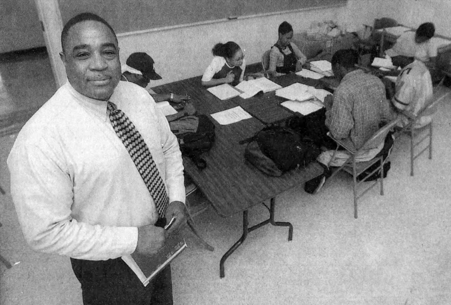Overhead shot of Weatherby smiling while students with open textbooks sit at a desk in the background