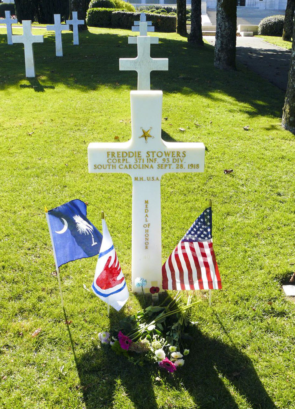 Cross marker with small flags and a bed of flowers in front of it