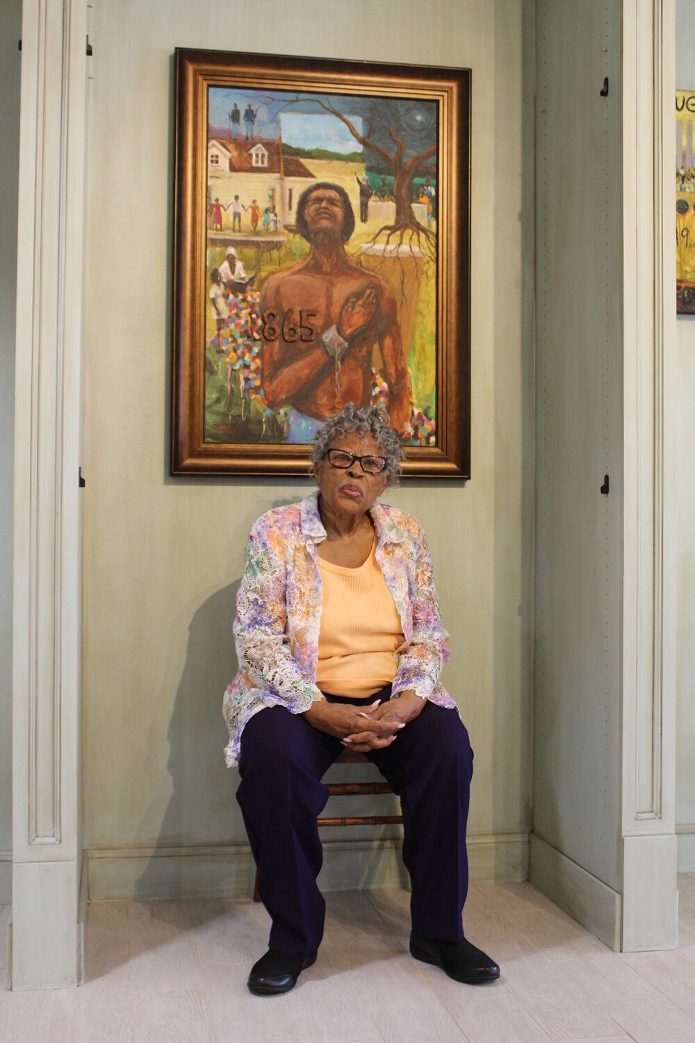 Lee seated in an alcove in front of a painting depicting a Black slave wearing broken chains and text reading "1865"