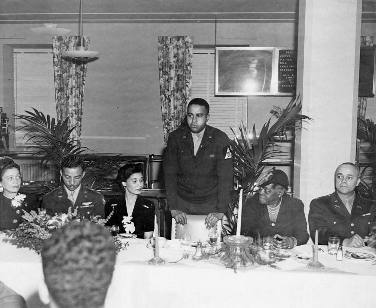 Moss leaning on a chair while speaking as five seated attendees listen