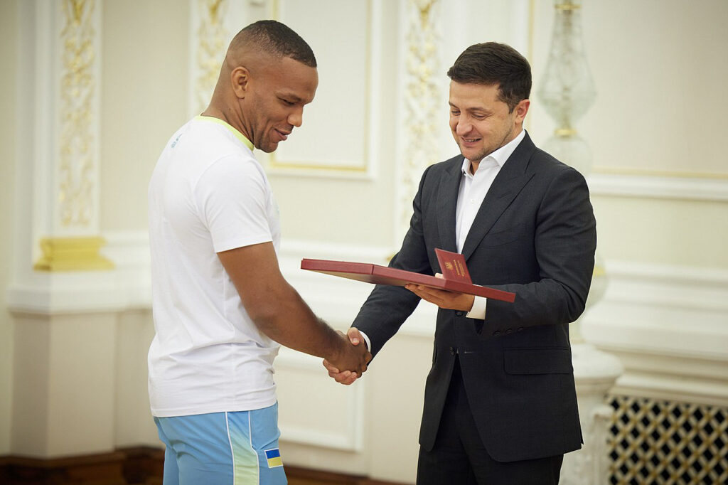 Two men shaking hands and smiling in an ornate white and yellow room
