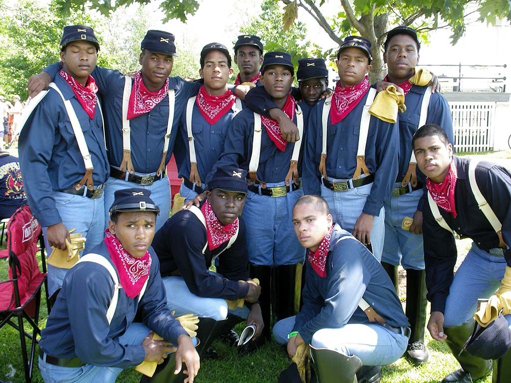 12 young men with blue shirts, blue jeans, blue caps, white suspenders, yellow gloves, and red bandanas around necks