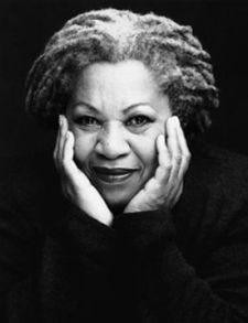 Black and white photo of Toni Morrison cradling her chin with her hands and smiling at the camera
