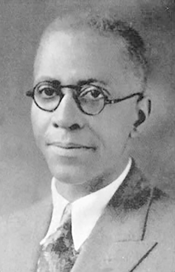 Coleman posing in rounded glasses, suit and tie